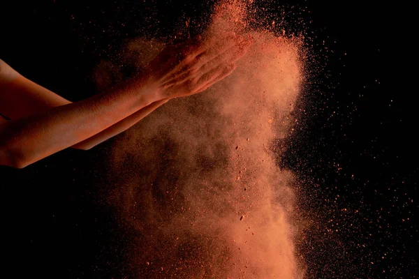 Corte vista de mãos femininas com laranja colorido holi pintura explosão no fundo preto — Fotografia de Stock