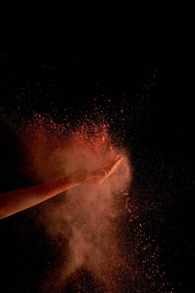 Corte vista da mão feminina com laranja colorido holi pintura explosão no fundo preto — Fotografia de Stock