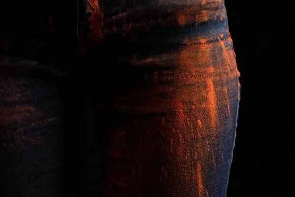 Cropped view of woman with orange colorful holi paint powder on jeans isolated on black — Stock Photo