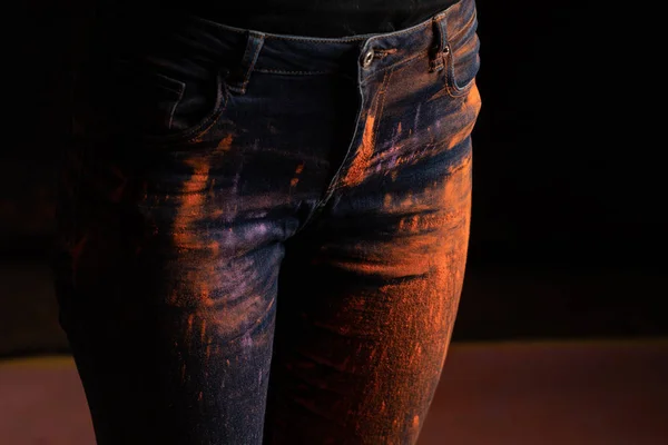 Vue recadrée de la femme avec de la poudre de peinture holi colorée orange sur jeans sur fond noir — Photo de stock