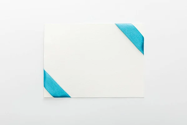 Vista superior de la tarjeta en blanco con cinta de satén decorativa azul sobre fondo blanco - foto de stock