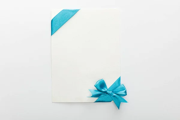 Top view of blank card with blue decorative satin ribbon and bow on white background — Stock Photo
