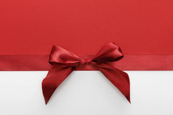 Top view of satin burgundy decorative ribbon with bow on white and red background — Stock Photo