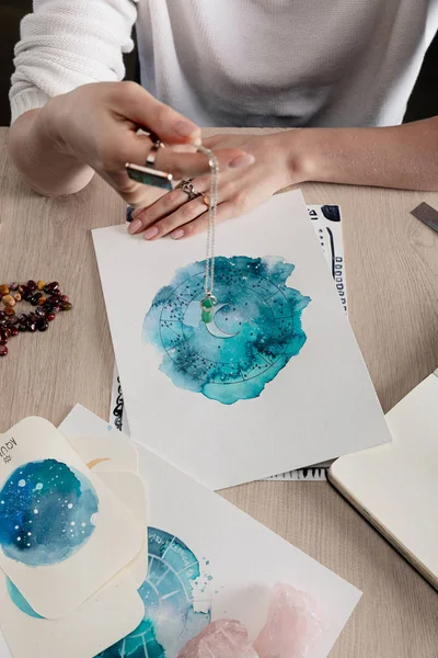 Vista cortada de astrólogo segurando cristal acima desenhos aquarela de signos do zodíaco em cartões na mesa isolado em preto — Fotografia de Stock