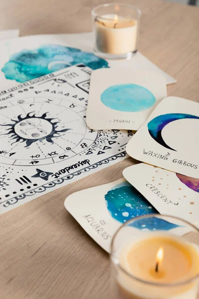 Selective focus of watercolor drawings with moon phases on cards and zodiac signs on wooden table with candles — Stock Photo