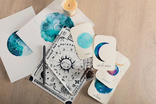 Top view of candle and cards with watercolor drawings of moon phases and zodiac signs on table — Stock Photo