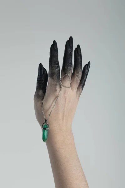 Vista recortada de la mano de bruja en pintura negra sosteniendo cristal aislado en gris - foto de stock