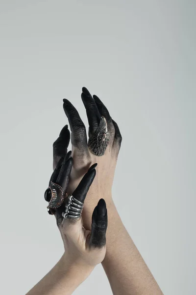 Cropped view of witch hands with black dye and jewelry rings isolated on grey — Stock Photo