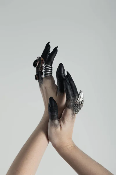 Cropped view of jewelry rings on witch hands with black paint isolated on grey — Stock Photo