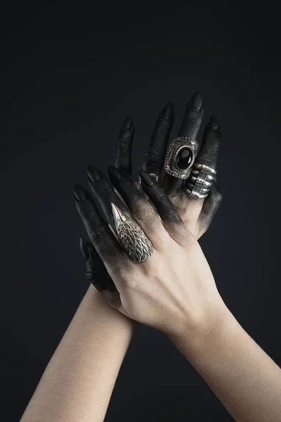 Cropped view of black painted hands of witch with jewelry rings isolated on black — Stock Photo