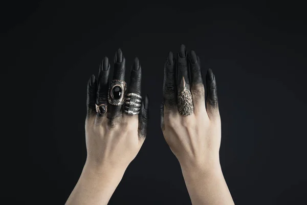 Cropped view of black painted hands of witch with jewelry rings isolated on black — Stock Photo
