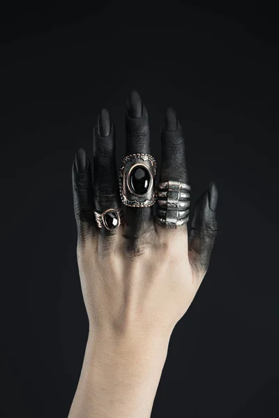 Cropped view of jewelry rings on black painted hand of witch isolated on black — Stock Photo