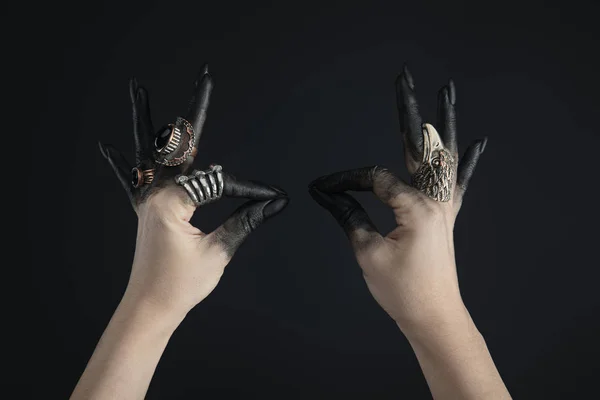 Cropped view of black painted hands of witch with jewelry rings isolated on black — Stock Photo