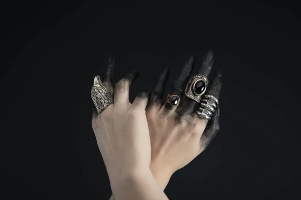 Обрезанный вид рук ведьмы с ювелирными кольцами и черной краской, изолированной на черном — стоковое фото