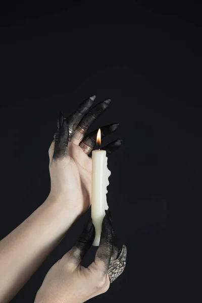 Cropped view of black painted witch hands holding burning candle isolated on black — Stock Photo