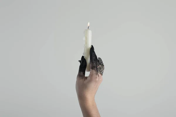 Cropped view of witch hand with jewelry ring and black paint holding candle isolated on grey with copy space — Stock Photo