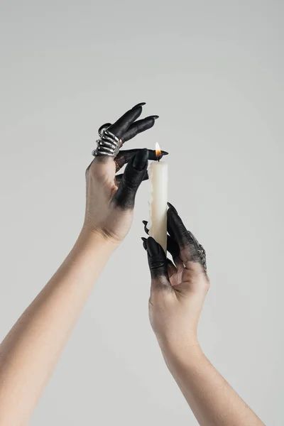 Cropped view of witch with black paint on hands holding burning candle isolated on grey — Stock Photo