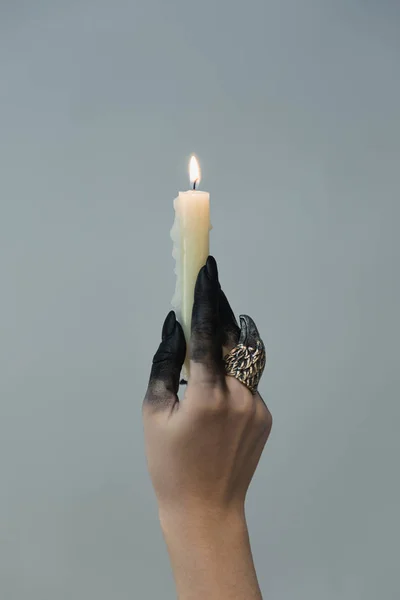 Vista recortada de bruja con tinte negro en la mano sosteniendo vela aislada en gris - foto de stock