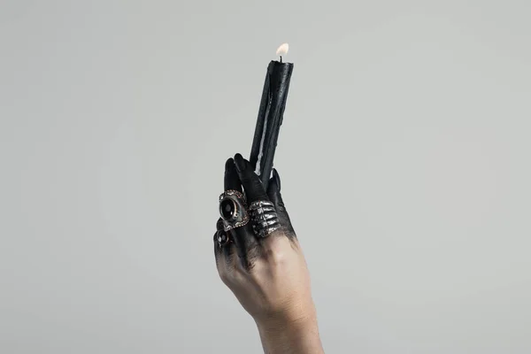 Cropped view of candle in black painted witch hand with jewelry rings isolated on grey — Stock Photo