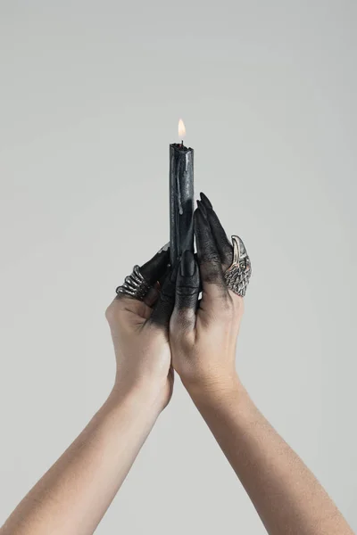 Обрізаний вид відьми з чорною фарбою на руках, що тримає палаючу свічку ізольовано на сірому — стокове фото