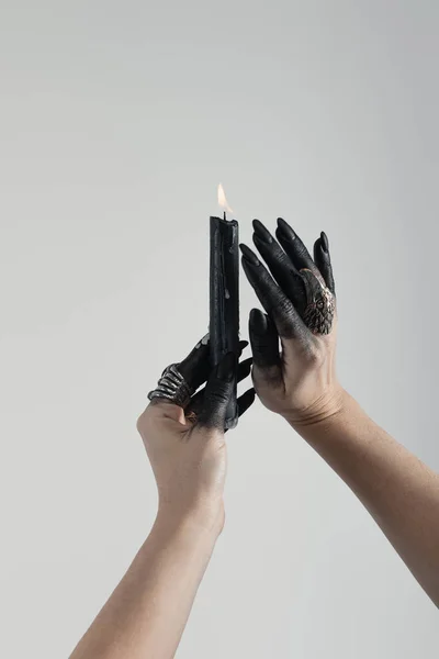 Cropped view of black painted hands of witch with jewelry rings and candle isolated on grey — Stock Photo