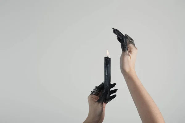 Cropped view of witch with black painted hands and jewelry rings holding candle isolated on grey with copy space — Stock Photo