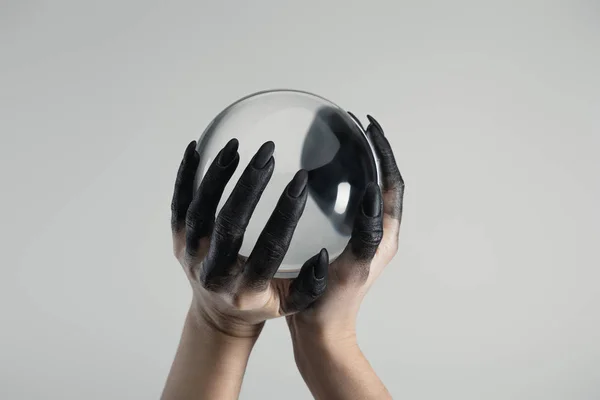 Cropped view of black painted hands of witch holding crystal ball isolated on grey — Stock Photo