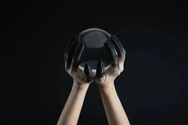 Vista cortada de mãos de bruxa em tinta preta segurando bola de cristal isolado em preto — Fotografia de Stock