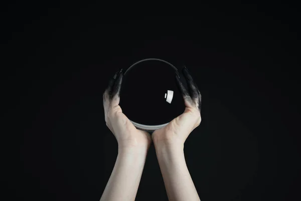 Vista recortada de bruja sosteniendo bola de cristal en manos pintadas negras aisladas en negro - foto de stock