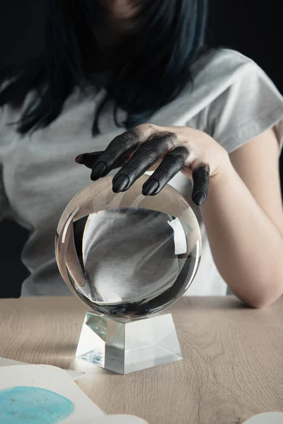 Cropped view of fortuneteller with black paint on hand holding crystal ball by watercolor painting on table isolated on black — Stock Photo