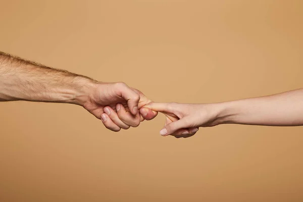 Vista recortada del hombre y la mujer sosteniendo los dedos aislados en beige - foto de stock