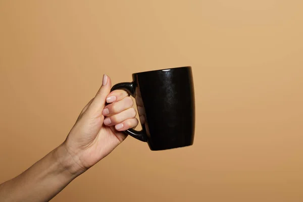 Vista ritagliata della donna che tiene la tazza nera isolata sul beige — Foto stock