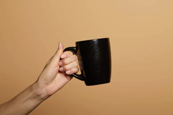 Vista cortada de mulher segurando caneca preta isolada no bege — Fotografia de Stock