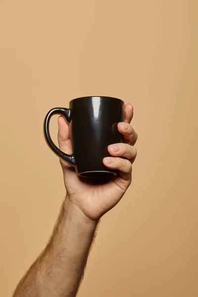 Vista ritagliata dell'uomo che tiene la tazza nera isolata sul beige — Foto stock