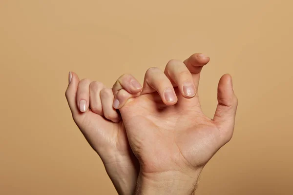 Cropped view of man and woman holding little fingers isolated on beige — Stock Photo