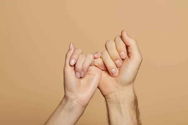 Cropped view of man and woman holding little fingers isolated on beige — Stock Photo