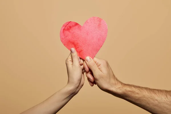 Vista recortada del hombre y la mujer sosteniendo el corazón rojo aislado en beige — Stock Photo