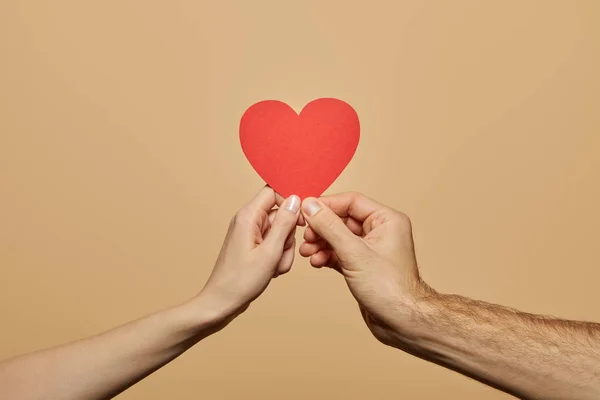 Vue recadrée de l'homme et de la femme tenant le cœur rouge isolé sur beige — Photo de stock