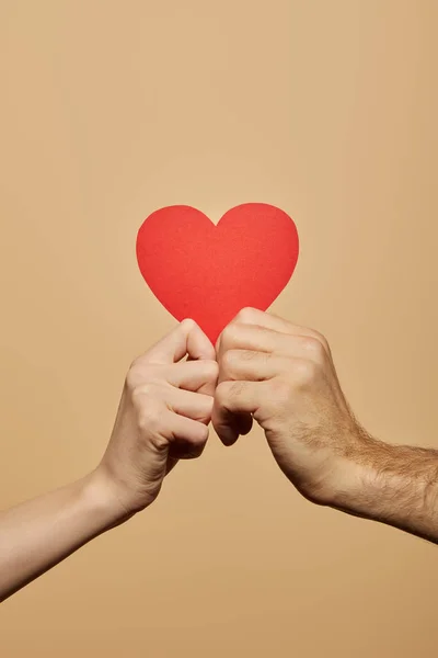 Vista recortada del hombre y la mujer sosteniendo el corazón rojo aislado en beige — Stock Photo
