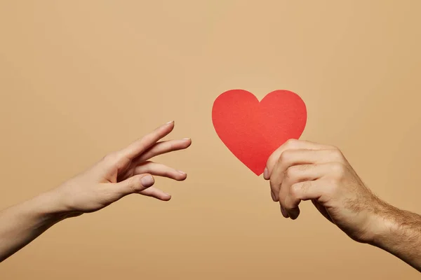 Vista recortada del hombre sosteniendo el corazón rojo y la mujer alcanzándolo aislado en beige — Stock Photo