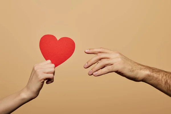 Vista recortada de la mujer sosteniendo el corazón rojo y el hombre alcanzándolo aislado en beige — Stock Photo