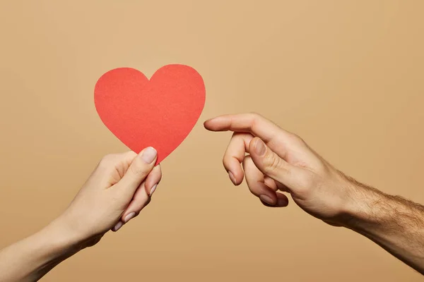 Cropped view of woman holding red heart and man reaching it isolated on beige — Stock Photo