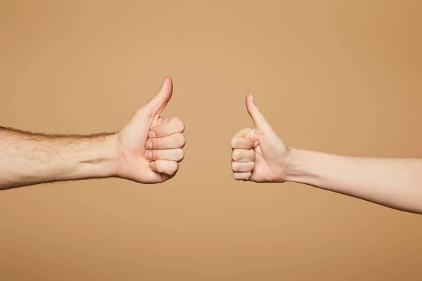 Recortado vista de hombre y mujer mostrando pulgares hacia arriba aislado en beige - foto de stock