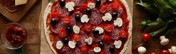 Top view of pizza with salami, mushrooms, olives and tomato sauce on wooden background, panoramic shot — Stock Photo