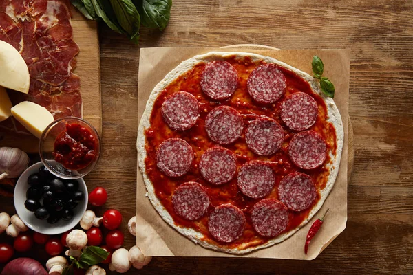 Top view of pizza with salami and tomato sauce on wooden background — Stock Photo