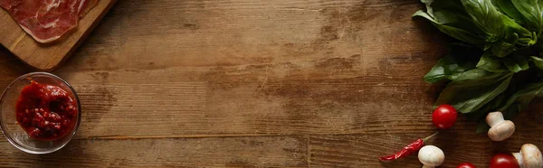 Vista dall'alto degli ingredienti per pizza con sugo di pomodoro, funghi, pomodorini, peperoncino e prosciutto su fondo di legno, colpo panoramico — Foto stock