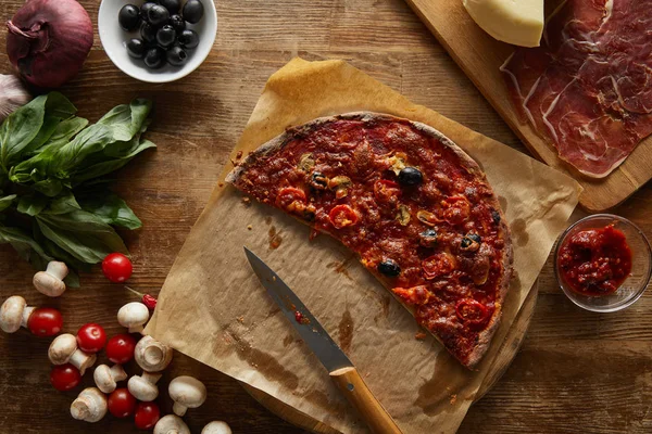 Vista superior de la deliciosa pizza sobre papel pergamino sobre fondo de madera — Stock Photo