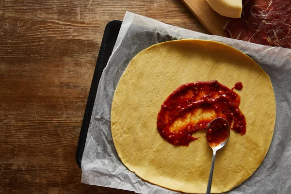 Vue du dessus de la pâte crue avec sauce tomate sur fond en bois — Photo de stock