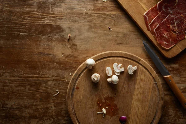 Top view of mushrooms, prosciutto and knife on wooden background — Stock Photo