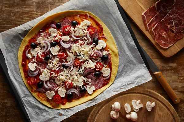 Vue de dessus de délicieuses pizzas sur papier parchemin, champignons et prosciutto sur fond de bois — Photo de stock